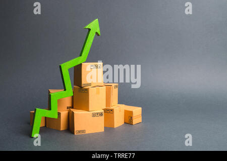 Ein Stapel von Kartons und einem grünen Pfeil nach oben. Das Wachstum der Produktion von Waren und Produkten, die zunehmende wirtschaftliche Indikatoren. Steigender Konsum Stockfoto