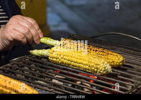 Frau hand Kochen gerösteten Mais auf einen Kohleofen closeup, im Freien. Stockfoto