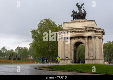 London, England, Großbritannien - 2. Mai 2019: Fußgänger und Radfahrer reisen durch den Hyde Park Corner bei starkem Regen Sturm in London. Stockfoto
