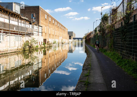 London, England, UK - 24. März 2019: ein Radfahrer fährt auf dem Leinpfad des Grand Union Canal neben industriellen Gebäuden im Park Royal Bereich Stockfoto