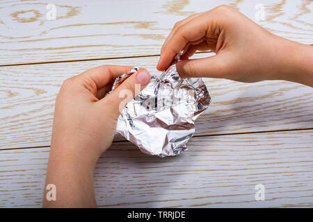 Hand reißen eine herzförmige Aluminiumfolie auf einer hölzernen Hintergrund Stockfoto