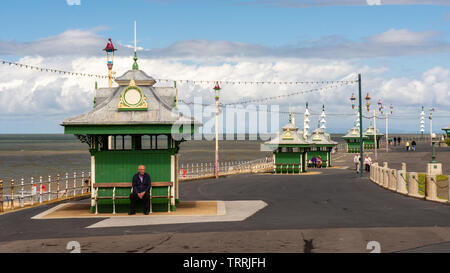 Blackpool, England, Großbritannien - 1 August 2015: ein Mann sitzt auf einer Bank in einem traditionellen Strandmuschel an der Promenade von Blackpool. Stockfoto