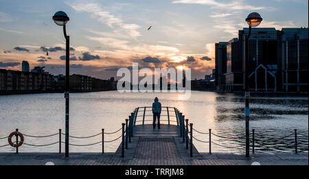 Die Silhouette eines jungen Mannes ein hoody mit Blick von der Kamera an einem Dock in Londons Docklands entfernt. Stockfoto