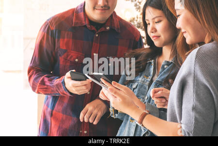 Drei jungen asiatischen Menschen mit und am Handy und Tablet-PC zusammen Stockfoto