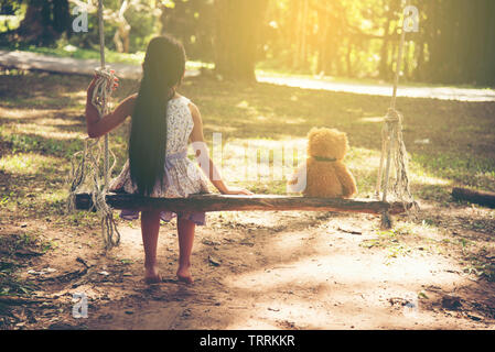 Kleine hübsche Mädchen und flauschigen Teddybär sitzen auf Holz- Swing im Park. Freundschaft Konzepte. Stockfoto