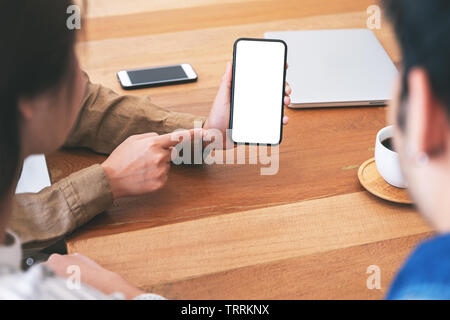 Menschen verwenden und gleichzeitig mockup Mobiltelefon auf hölzernen Tisch zusammen suchen Stockfoto