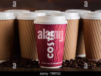 LONDON, UK - Juni 05, 2019: Costa Pappbecher für nehmen Sie mit Kaffeebohnen auf Holzuntergrund mit leeren Kaffeetassen. Stockfoto