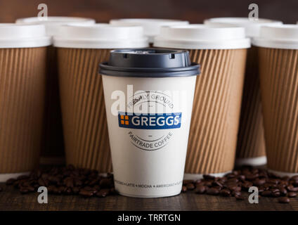 LONDON, UK - Juni 05, 2019: Greggs Kaffee Pappbecher für nehmen Sie mit Kaffeebohnen auf hölzernen Hintergrund mit braunen Kaffee Tassen. Stockfoto