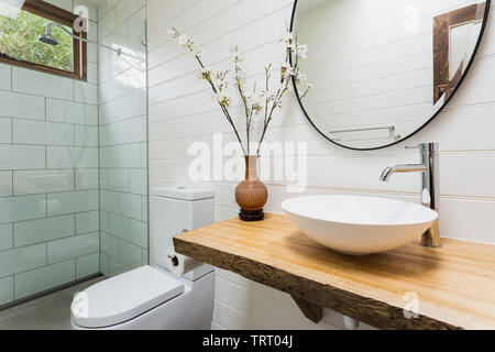 Badezimmer mit Waschbecken, Holzbank, runde, schwarze Spiegel und Dusche Stockfoto