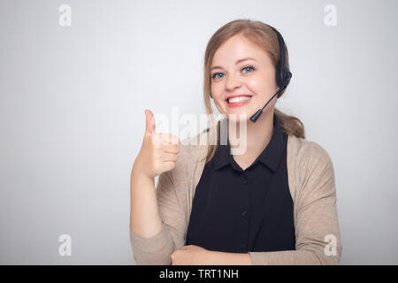 Glücklich lächelnde Junge kaukasier Frau mit Headset Telefon in einem Call Center, Daumen hoch Stockfoto