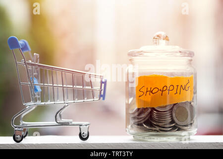 Geld sparen für Shopping Haushalt, Münzen halten im Glas mit Warenkorb Stockfoto