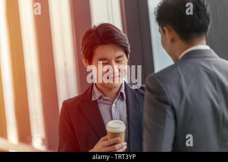 Jungen Asiatischen leader Geschäftsmann professionelles Aussehen zusammen gesprochen im Büro mit heißem Kaffee Becher in der Hand Stockfoto