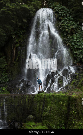 Ein Mann erforscht neue, magisch, und fantastischen Orten rund um die Welt ist vor einem Wasserfall, umgeben von Natur und ist auf der Suche nach oben und Entspannen. Stockfoto