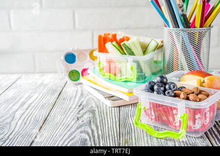 Gesunde Schule Lunch Box. Kid's Lunch Box mit Sandwiches, Obst, Gemüse, Nüssen, Wasser- und Schulbedarf, weiß Holz- Hintergrund Stockfoto