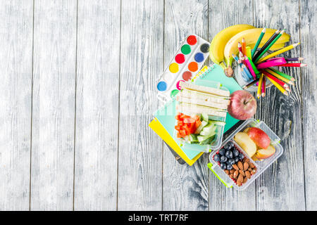 Gesunde Schule Lunch Box. Kid's Lunch Box mit Sandwiches, Obst, Gemüse, Nüssen, Wasser- und Schulbedarf, weiß Holz- Hintergrund Stockfoto