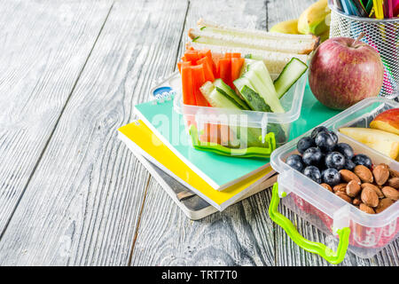 Gesunde Schule Lunch Box. Kid's Lunch Box mit Sandwiches, Obst, Gemüse, Nüssen, Wasser- und Schulbedarf, weiß Holz- Hintergrund Stockfoto