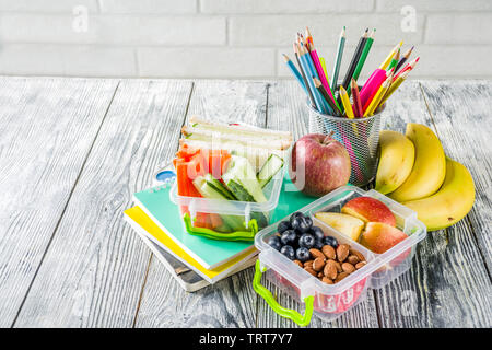 Gesunde Schule Lunch Box. Kid's Lunch Box mit Sandwiches, Obst, Gemüse, Nüssen, Wasser- und Schulbedarf, weiß Holz- Hintergrund Stockfoto