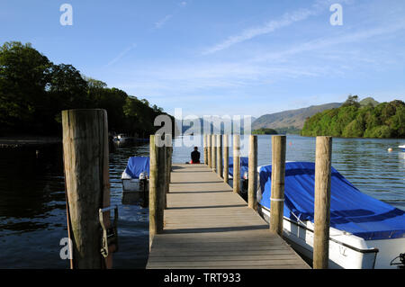 Eine einsame Gestalt sitzt am Ende einer der Stege auf Derwentwater im englischen Lake District. Er ist auf der Suche nach Borrowdale. Stockfoto