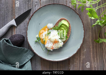 Avocado Sandwich mit dunkles Brot, geschnitten Avocado und pochiertem Ei, flach auf rustikalen hölzernen Hintergrund Stockfoto