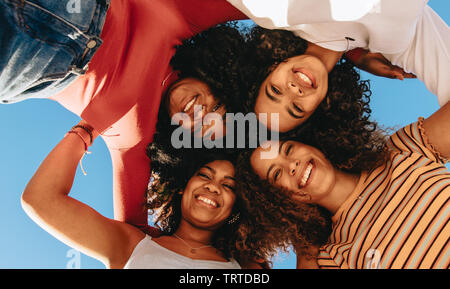 Ansicht von unten der Gruppe der Glückliche junge Mädchen mit lockigem Haar stehen im Kreis und auf Kamera. Lächelnd Freunde in eine Hürde. Stockfoto