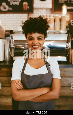 Zuversichtlich, dass weibliche Barista vor einem Cafe. Frau cafe Eigentümer im Vorfeld auf Kamera und lächelnd mit verschränkten Armen. Stockfoto