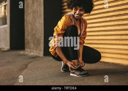 Frau, die Schnürsenkel bindet und lächelt. Fitness-Frau, die sich morgens zum Laufen bereit macht. Stockfoto