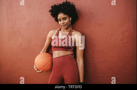 Fitness-Frau, die sich nach dem Training entspannt und mit Basketball steht. Frau in Fitnesskleidung entspannend nach Basketballtraining. Stockfoto