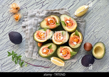 Avocado Boote mit geräuchertem Lachs, Zitrone, Physalis und Minzeblatt, Ansicht von oben an der strukturierten Hintergrund Stockfoto