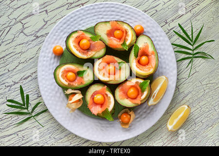 Avocado Boote mit geräuchertem Lachs, Zitrone, Physalis und Minzeblatt, Ansicht von oben an der strukturierten Hintergrund Stockfoto