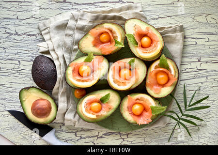 Avocado Boote mit geräuchertem Lachs, Zitrone, Physalis und Minzeblatt, Ansicht von oben an der strukturierten Hintergrund Stockfoto