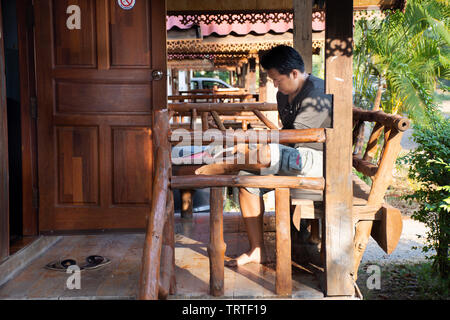 Reisende thai Mann sitzt entspannt Buch an den hölzernen Hütte von Resort und Homestay nach Mieten und Rest in morgen mal in die Stadt von phraya Lae. Stockfoto