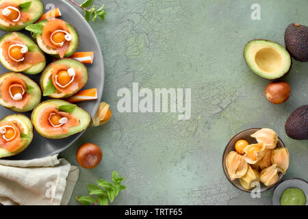 Avocado Boote mit geräuchertem Lachs, Zitrone, Physalis und Minzeblatt, Ansicht von oben auf die Grüne strukturierten Hintergrund mit copy-Raum Stockfoto