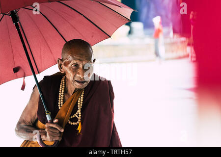 Yangon, Myanmar - März 2019: Portrait des alten buddhistischen Mönch mit roten Regenschirm in der Shwedagon Pagode. Stockfoto