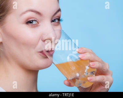 Ernährung, Gesundheit Konzept. Frau mit Glas orange aromatisierte Getränke und Trinken aus. Studio shot auf blauem Hintergrund Stockfoto