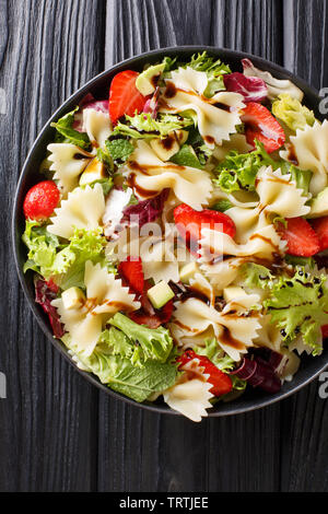 Farfalle Nudeln mit Avocado, Erdbeeren, Salat und Balsamico-dressing close-up auf einem Teller auf den Tisch. Vertikal oben Ansicht von oben Stockfoto