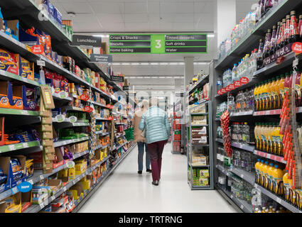 Zwei ältere Frauen Gang angezeigte Produkte: alkoholfreie Getränke, Kekse und Chips in Asda Supermarkt, Großbritannien Stockfoto