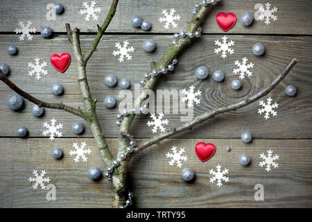 Original Weihnachtsbaum Konzept mit Blattlosen Zweig, silber Brokat pellets, Silber Perlen Kette, rote Herzen und Schneeflocken auf Holzplatten Stockfoto