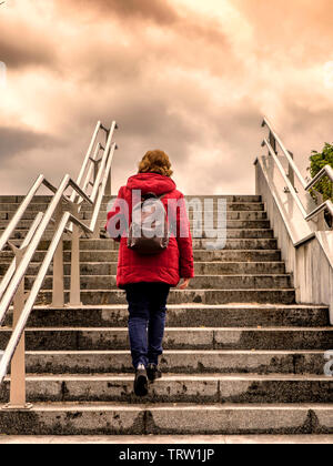 Frau mit roten Mantel zu Fuß die Treppe zum bewölkte Himmel Stockfoto