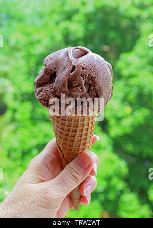 Hand mit Schokolade Eis in Kegel gegen Blurry Sunshine Garden Stockfoto