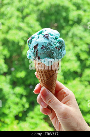 Vertikale Bild von Hand mit Mint Choc Chip Eis in Kegel gegen Blurry Sunshine Garden Stockfoto
