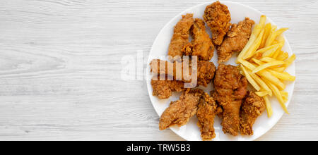 Lecker gebratene Hähnchenschenkel, würzige Flügel, Pommes frites und Chicken Streifen auf einer weißen Platte über weiße Holz- Oberfläche, Ansicht von oben. Flach, Overhead, aus Stockfoto