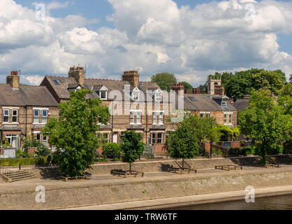 Eine Reihe von Reihenhäusern entlang des Flusses Ouse in York. Ein Kirchturm ist hinter den Häusern und Bäumen auf der einen Seite sammeln. Stockfoto