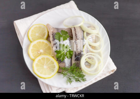 Köstliche Ausschreibung Hering Filet mit Zitrone, grünen und Zwiebeln auf einem weißen Teller auf einem dunklen Hintergrund Stockfoto