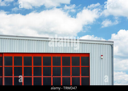 Hangar außen mit roten Tor unter einem blauen Himmel. Weiß Airport Hangar mit einem roten Tor, Teilansicht Stockfoto