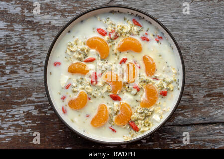 Frisches Frühstück mit Müsli, Joghurt, Nüsse, Goji Beeren, Chia Samen und Mandarin. Müsli mit Früchten und Beeren in der Schüssel auf einer hölzernen Hintergrund, in der Nähe Stockfoto