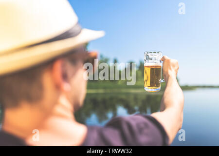 Ansicht der Rückseite des hipster Guy holding Bierkrug gegen schönen See im Hintergrund. Freiheit Konzept. Stockfoto