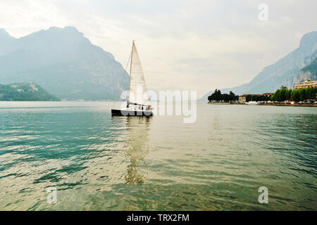 Schöner Panoramablick in die Hintergrundbeleuchtung an den Comer See in Lecco mit Segelboot Navigation von der Stadt bei Sonnenuntergang im Frühjahr. Stockfoto