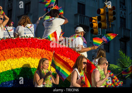 NEW YORK CITY - 25. Juni 2017: Die Teilnehmer tragen Wyndham und Barclays shirts wave Flags auf einem Schwimmer, der mit einem Regenbogen Bogen an der Gay Pride Parade. Stockfoto