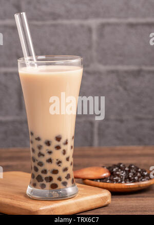 Beliebte Taiwan Getränk - Bubble Milch Tee mit Tapioka Perlen Kugel in Glas und Stroh, Holz- Tabelle grau Ziegelstein Hintergrund, Nahaufnahme, kopieren Raum Stockfoto