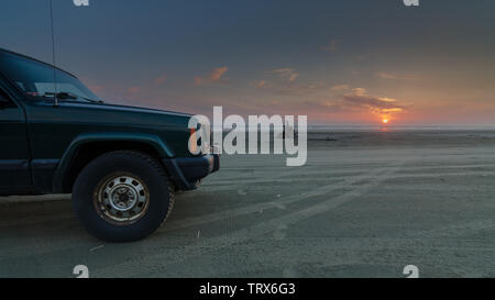 Grüne SUV am Strand mit Sonnenuntergang Stockfoto